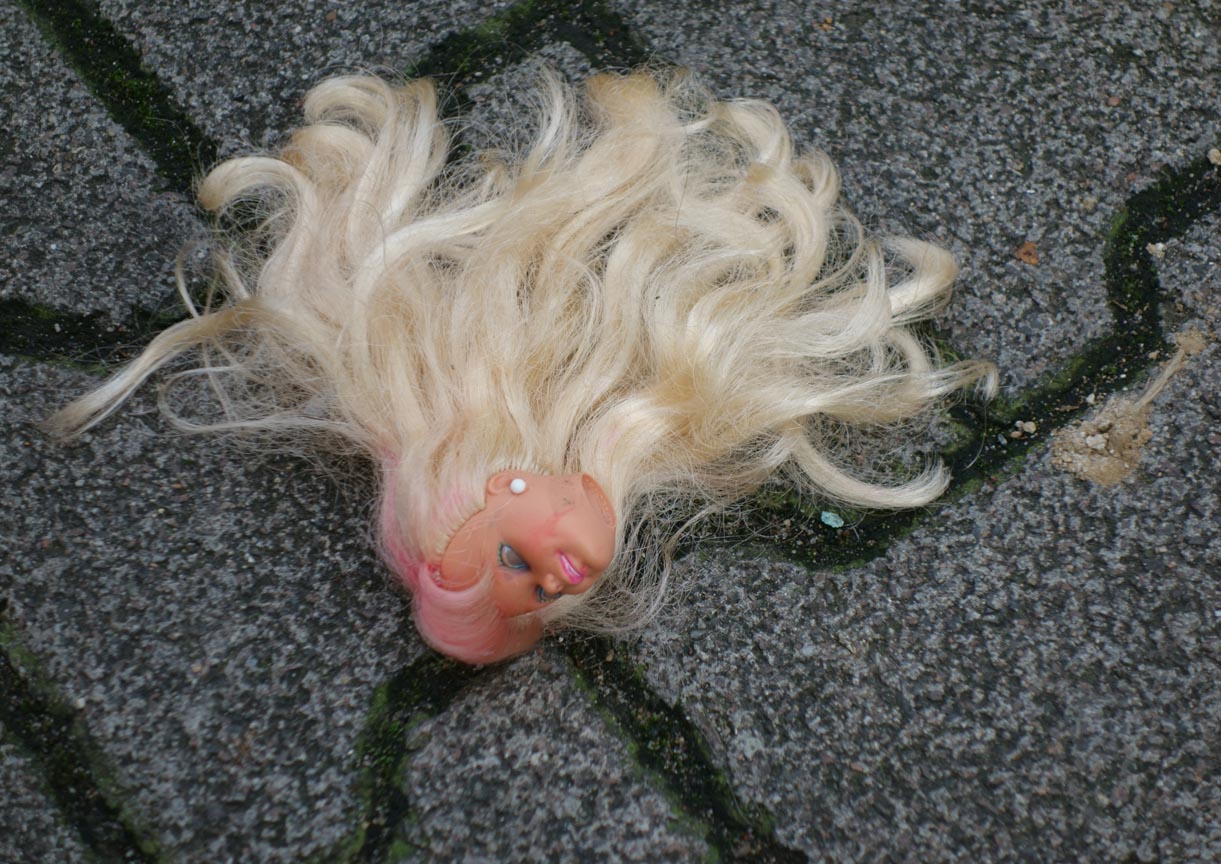 Abgetrennter Kopf einer Barbie-Puppe auf der Straße; Photo